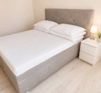 Postel s nočním stolkem a lampou v 2-pokojovém bytě na podlaze s dřevěným dekorem.