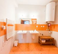 Koupelna v 3-pokojovém bytě s oranžovými kachličkami, dvěma umyvadly a bojlerem.