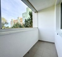 Balkon s dlaždicovou podlahou ve 3-pokojovém bytě, s výhledem na okolní zeleň.
