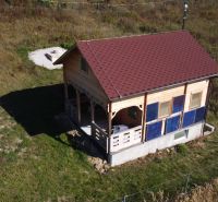 Chata v Horní Breznici s dřevěným obkladem a červenou střechou na zeleném pozemku.