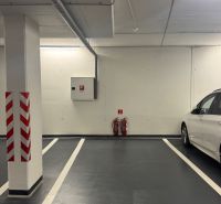 Podzemní parkovací místo s jasným značením a bílým autem vedle.