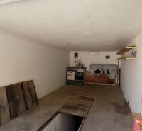 Garáž s policemi, cestní podlahou, regály a uloženými předměty.