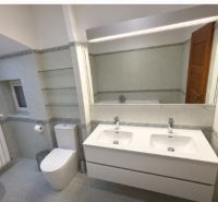 Koupelna v rodinném domě s dvojitým umyvadlem, WC a zrcadlem.