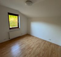 Pokoj v rodinném domě s podlahou s dřevěným dekorem a radiátorem pod oknem.