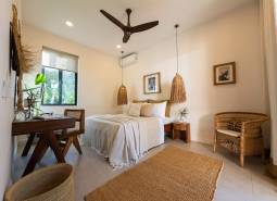 Světlá ložnice se závěsnými lampami a proutěným nábytkem v rodinném domě.