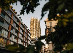 Výšková budova v pozadí ulice se zelení a bytovými jednotkami v Bratislavě.
