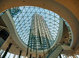 Prostorné atrium se skleněnou střechou a vysokou budovou v pozadí.