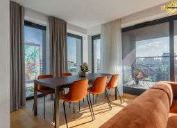 Jídelní kout s oranžovými židlemi, podlaha s dřevěným dekorem, výstup na balkon. Výstavba bytů.