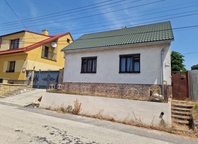Rodinný dům ve Štefanově s bílou omítkou a zelenou střechou na tiché ulici.