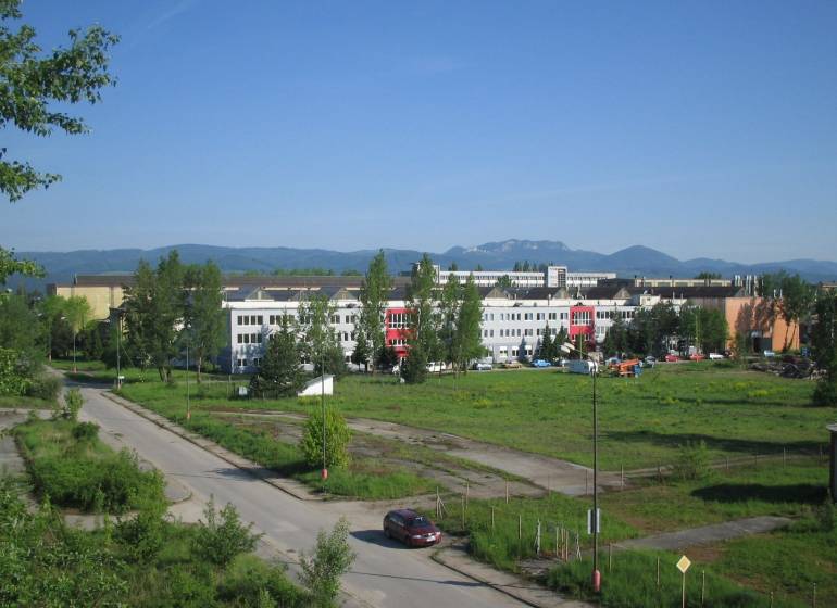Budova na pozemku v Dubnici nad Váhom; komerční využití s okolní přírodou a cestou.