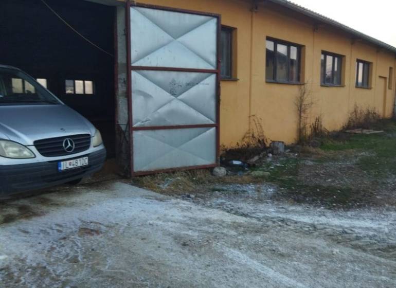 Obrázek z Ladiec zobrazuje sklady a haly s automobilem u otevřené brány.