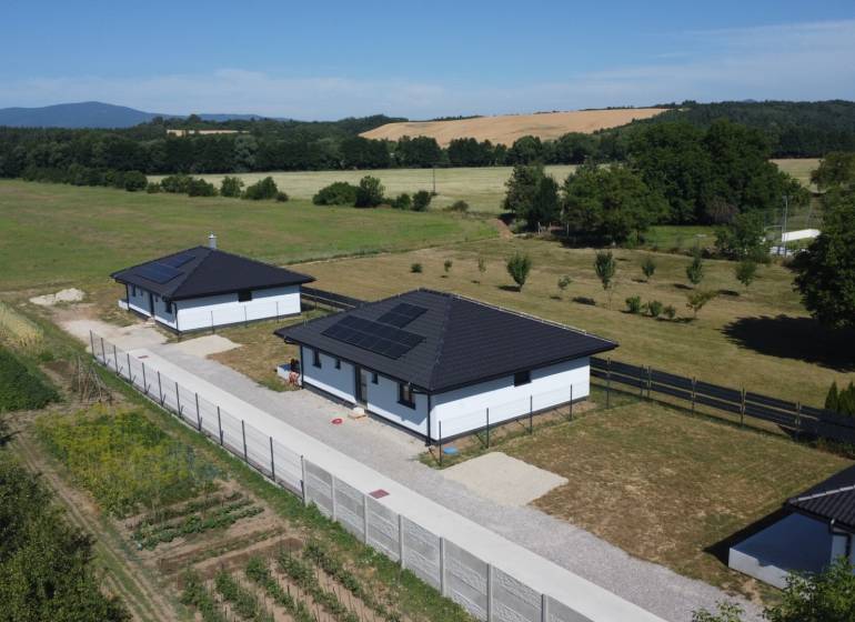 Rodinné domy v Podlužanech s moderními střechami a solárními panely na poli.