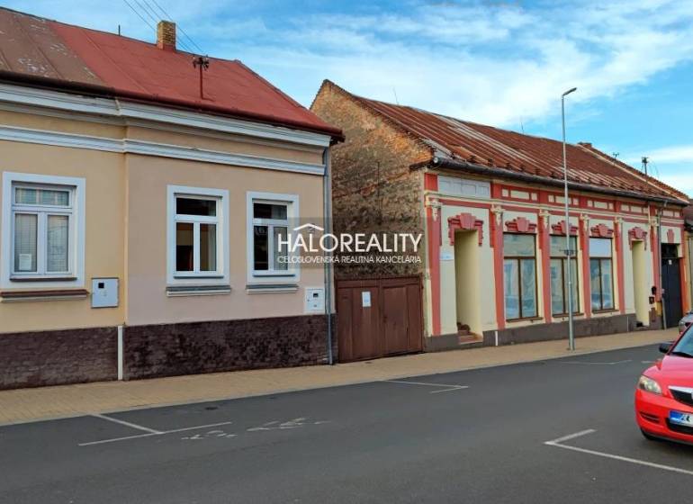 Rodinný dům v Lučenci se staršími fasádami a zaparkovaným červeným autem na ulici.