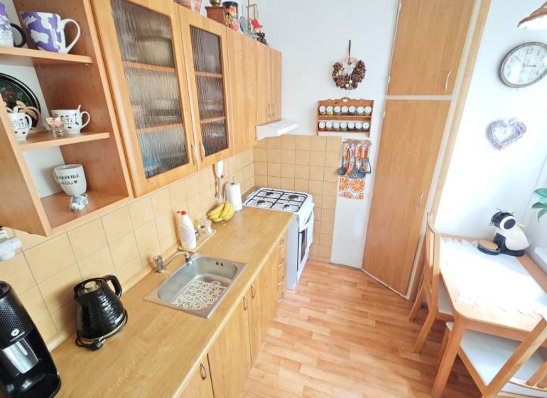 Kuchyně v 2pokojovém bytě s dřevěným nábytkem, jídelním koutem a dekoracemi.