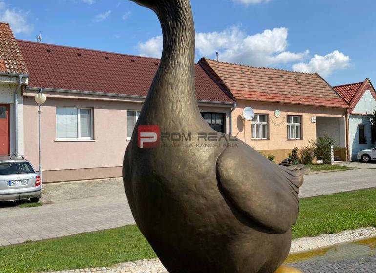 Socha husy se pozlaceným vejcem, na ulici Slovenský Grob, v pozadí jsou sklady a haly.
