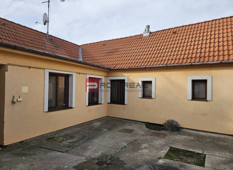 Dvůr rodinného domu na Sluneční ulici v Pezinku s betonovou dlažbou a oranžovou fasádou.