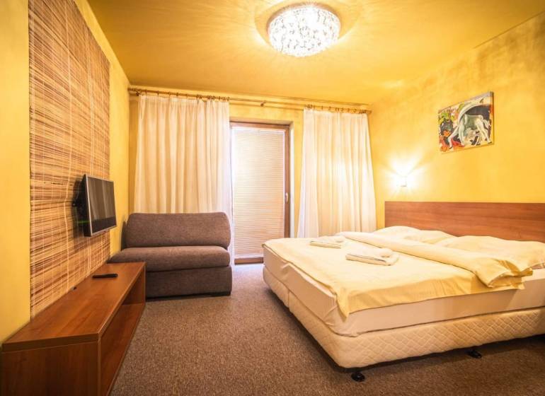 Ložnice v rekreačním apartmánu s manželskou postelí, pohovkou a televizí.
