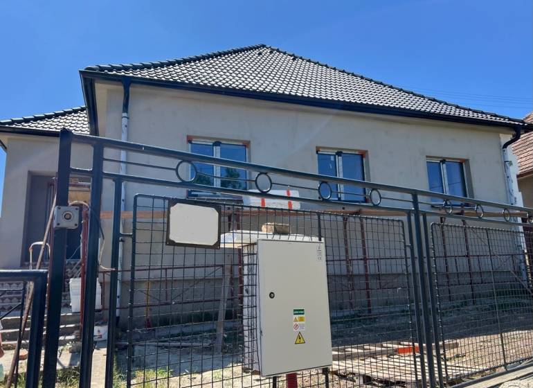 Rodinný dům v Sasinkově na ulici Sasinkovo s nedokončenou fasádou za kovovým plotem.