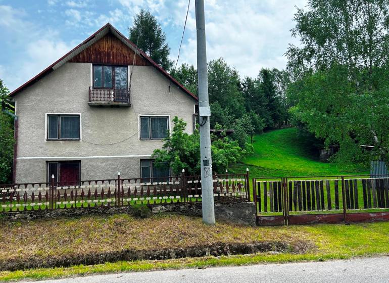 Rodinný dům ve Velké Lesné s upravenou zahradou a trávníkem, obklopený stromy.