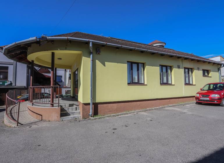 Žlutá budova s parkovištěm a autem na ulici Slovenského národního povstání ve Vrbovém.