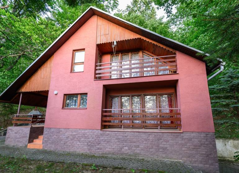 Dřevěná chata v Ružiné, obklopená zelení a s terasou v patře.