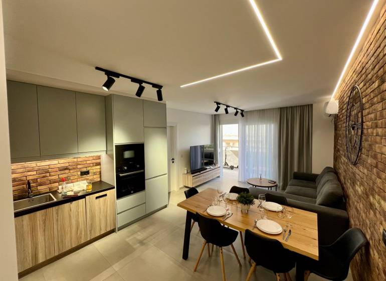 Obývací pokoj s kuchyní v rekreačním apartmánu. Cihlová stěna, jídelní stůl a pohodlná sedačka.