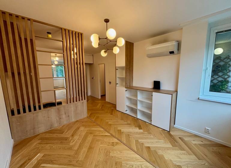 Interiér 2-pokojového bytu s dřevěnou podlahou, dělicí stěnou a moderním osvětlením.