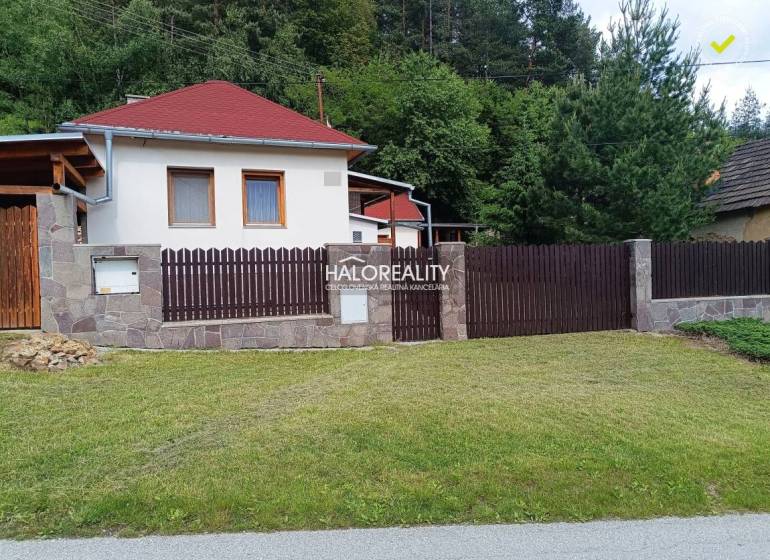 Chata v Helcmanovcích s dřevěným plotem a upraveným trávníkem obklopená zelení.