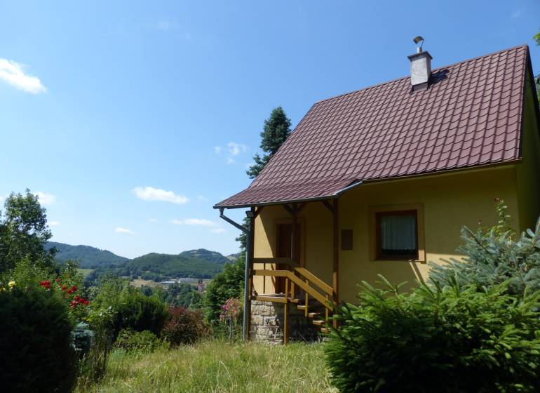 Chata v Štiavnických Baniach, obklopená zelení a s výhledem na kopce v pozadí.