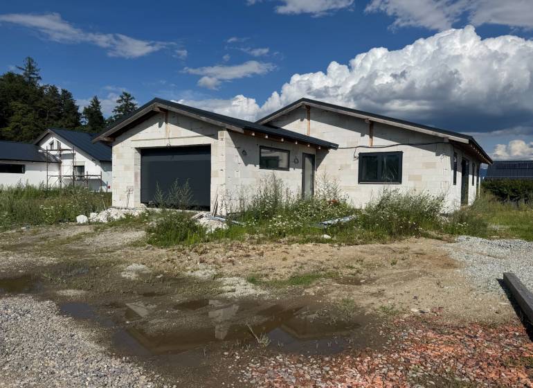 Nedokončený rodinný dům ve Valči s garáží obklopený přírodou a stavebním materiálem.
