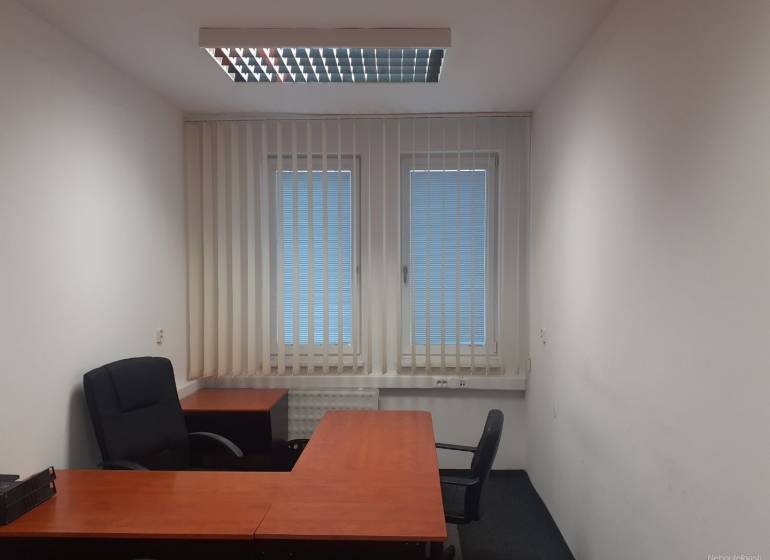 Kanceláře se stoly, černými židlemi a žaluziemi na oknech.