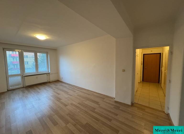 Prostorný pokoj s laminátovou podlahou v 2pokojovém bytě, sluneční světlo přes velké okno.