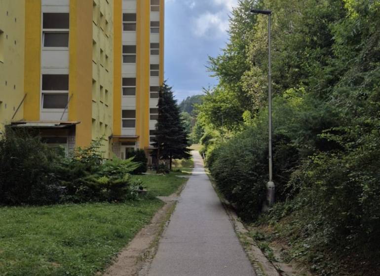 Žlutý bytový dům na Moskevské ulici v Banské Bystrici vedle chodníku a zeleně.
