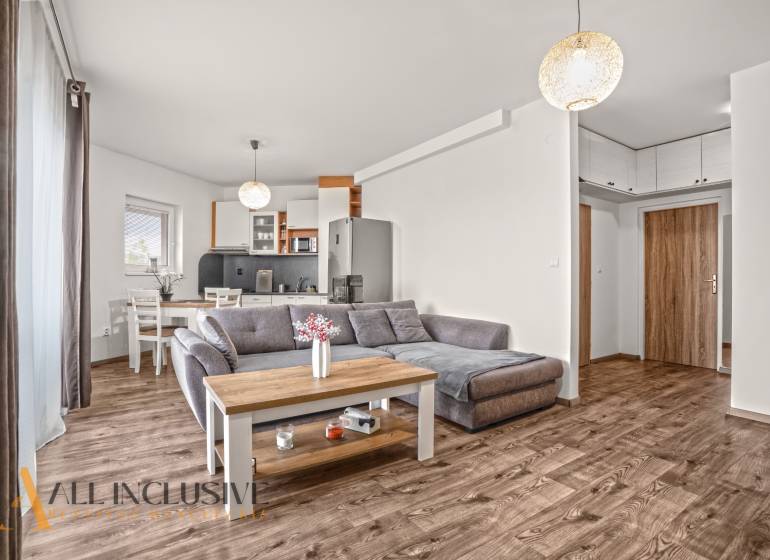 Obývací pokoj dvoupokojového bytu s pohovkou a podlahou s dřevěným dekorem.