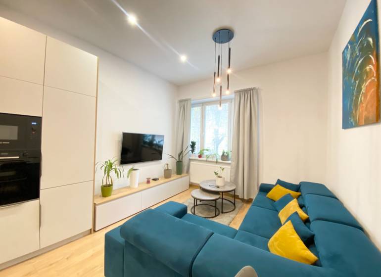 Obývací pokoj v 2-pokojovém bytě s modrou sedačkou a podlahou s dřevěným dekorem.