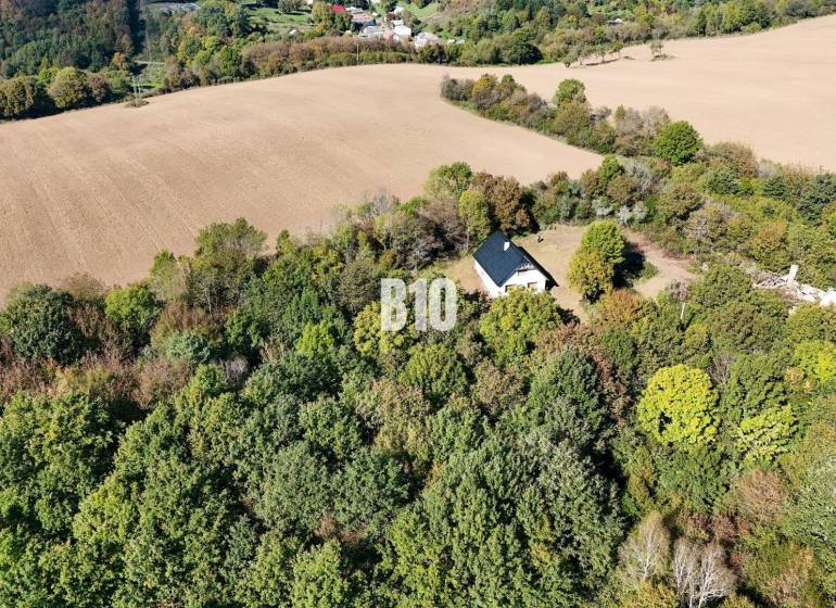 Chata v Lackově obklopená lesem a poli, klidná venkovská krajina.