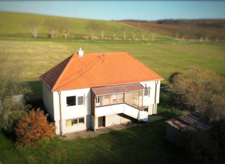 Rodinný dům v Dobré Vodě se šikmou střechou, obklopený zelení a loukami.