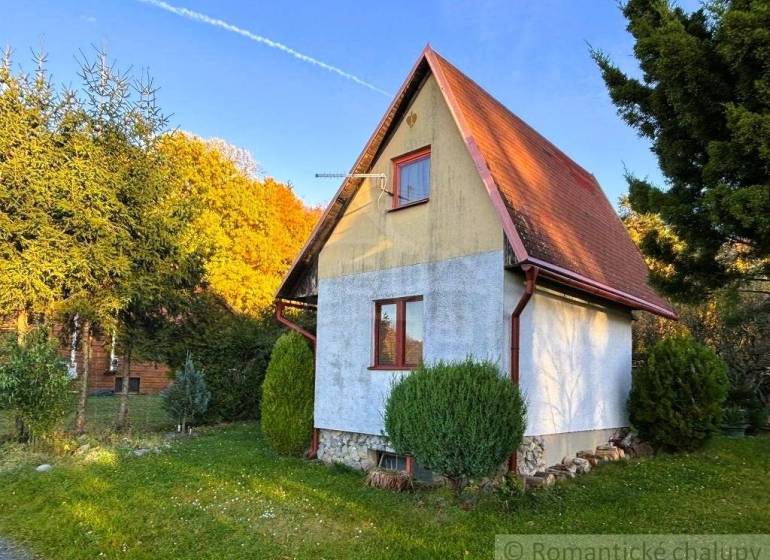 Chata v Sološnici obklopená zelení, se sedlovou střechou a udržovaným trávníkem.