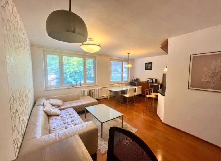 Obývací pokoj v 3-pokojovém bytě s pohovkou, stolem a jídelním koutem.