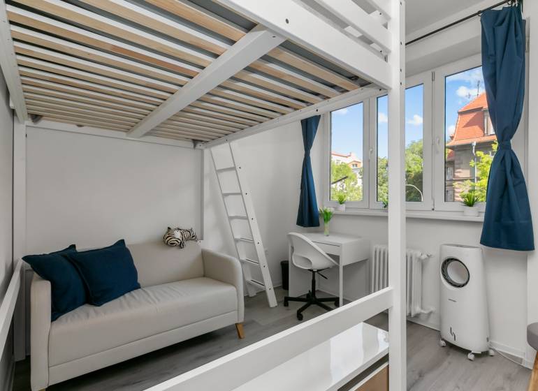 Garsonka s patrovou postelí, pracovním koutem a pohovkou, podlaha s dřevěným dekorem.