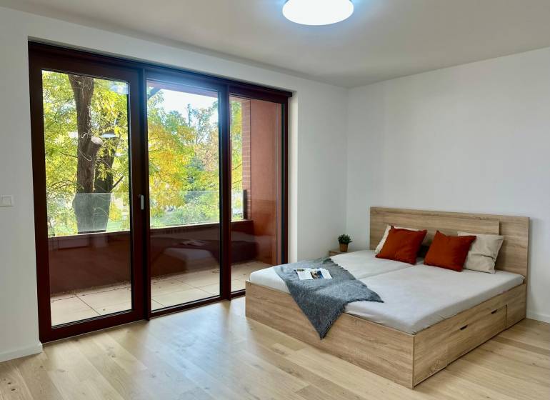 1pokojový byt s velkými okny, podlaha s dřevěným dekorem, balkon a postel.