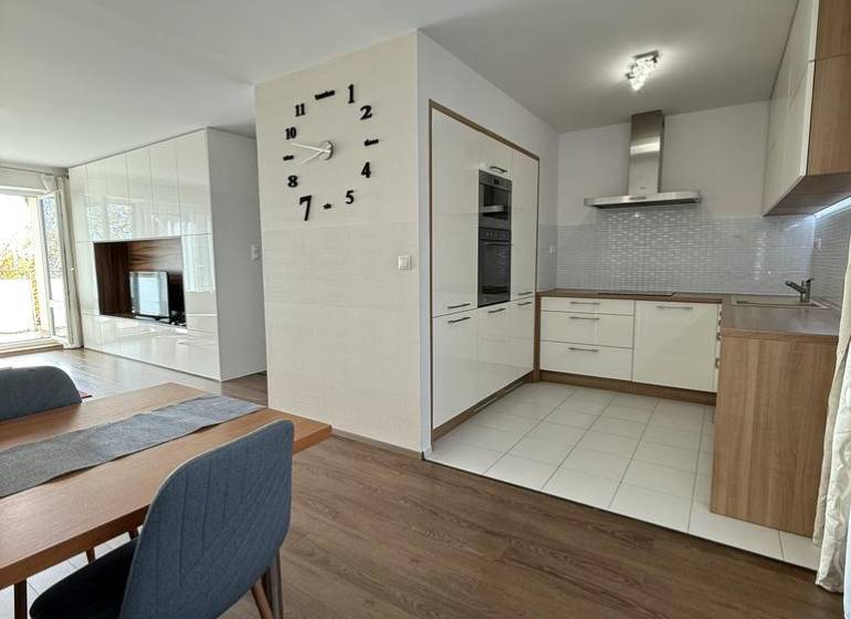 Jídelní prostor ve 4-pokojovém bytě s podlahou s dřevěným dekorem a kuchyní v pozadí.