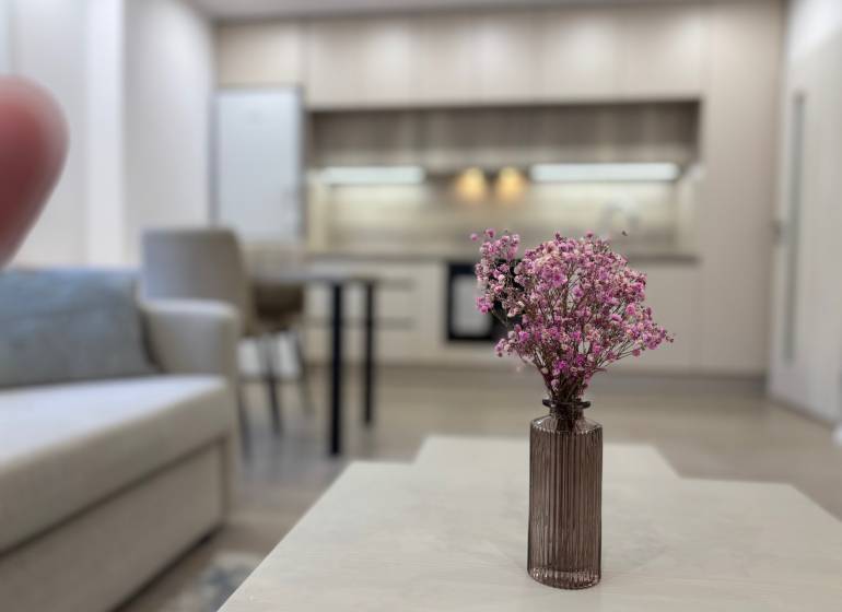 Obývací pokoj s kuchyní a květinami na stole v 2-pokojovém bytě.