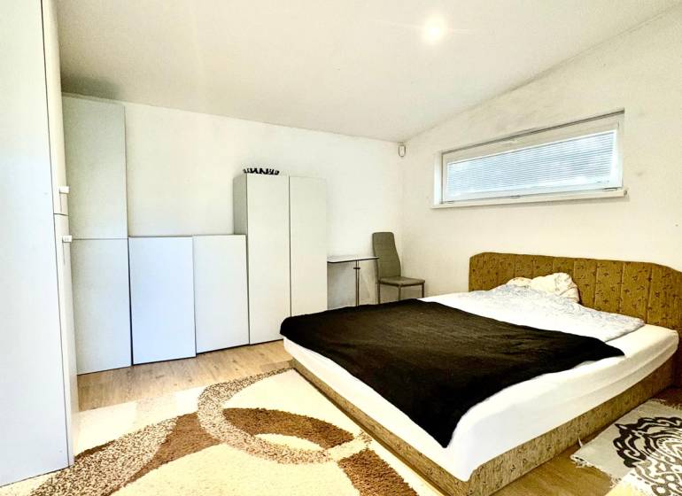 Ložnice v rodinném domě s postelí, skříňkami a podlahou s dřevěným dekorem.