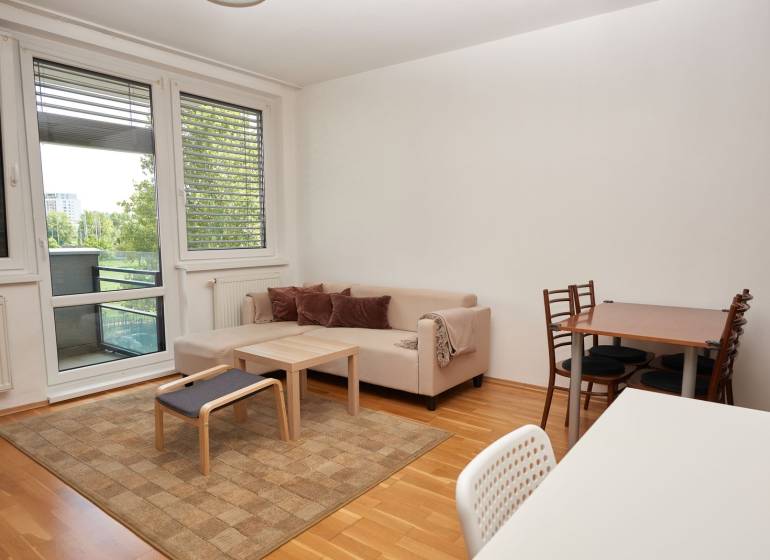 Obývací pokoj s pohovkou, jídelním stolem a podlahou s dřevěným dekorem ve 2pokojovém bytě.