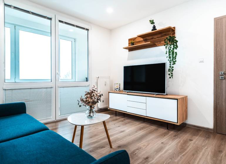 Obývací pokoj v 2-pokojovém bytě s pohovkou, televizí a podlahou s dřevěným dekorem.