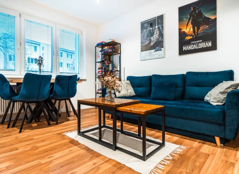 Obývací pokoj v 2-pokojovém bytě s modrou sedačkou a podlahou s dřevěným dekorem.