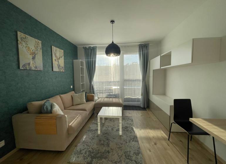 Obývací pokoj 1+kk s pohovkou, dekorací jelena a podlahou s dřevěným dekorem.