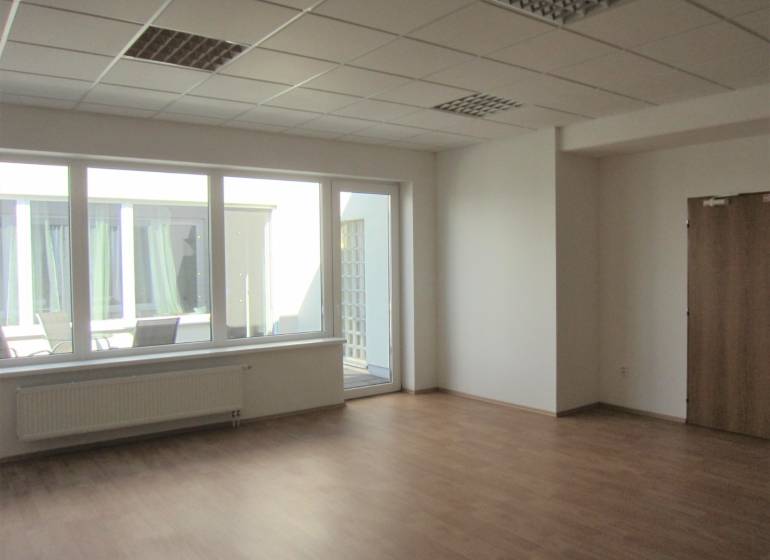 Prostorná kancelář s velkými okny a podlahou s dřevěným dekorem.