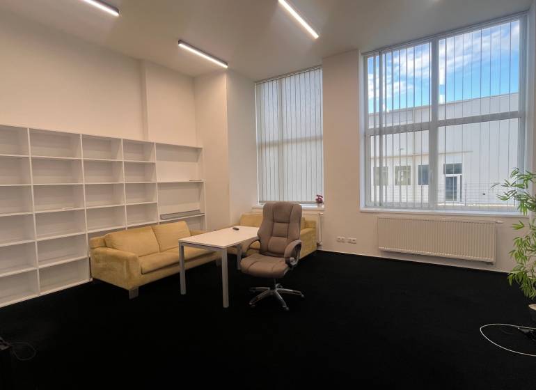 Kanceláře s černým kobercem, nábytkem, policovými systémy a velkými okny.